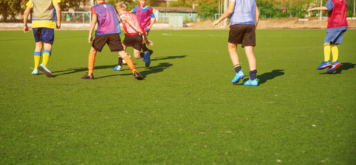 Fototapeta premium The photo shows a group of young soccer players in action on a green artificial turf field. They wear colorful jerseys and soccer gear, engaging in a sports practice or friendly match.