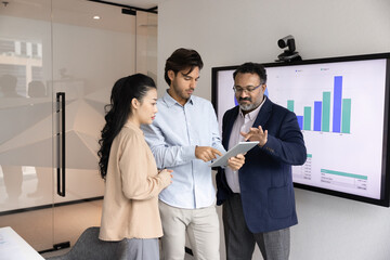 Multiethnic team of business colleagues using tablet in meeting room, analyzing website ecommerce...