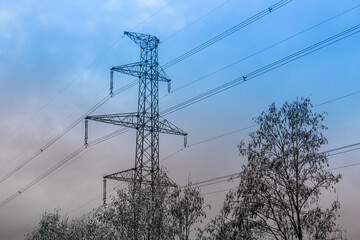 High-voltage electricity pylons stretch across a snowy landscape alongside a winding road under a blue winter sky. The scene captures the contrast between industrial infrastructure and nature.