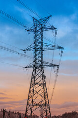 A high-voltage electricity pylon with power lines stretching across the sky during dusk. The silhouette contrasts with the gradient hues of blue and orange in the background.