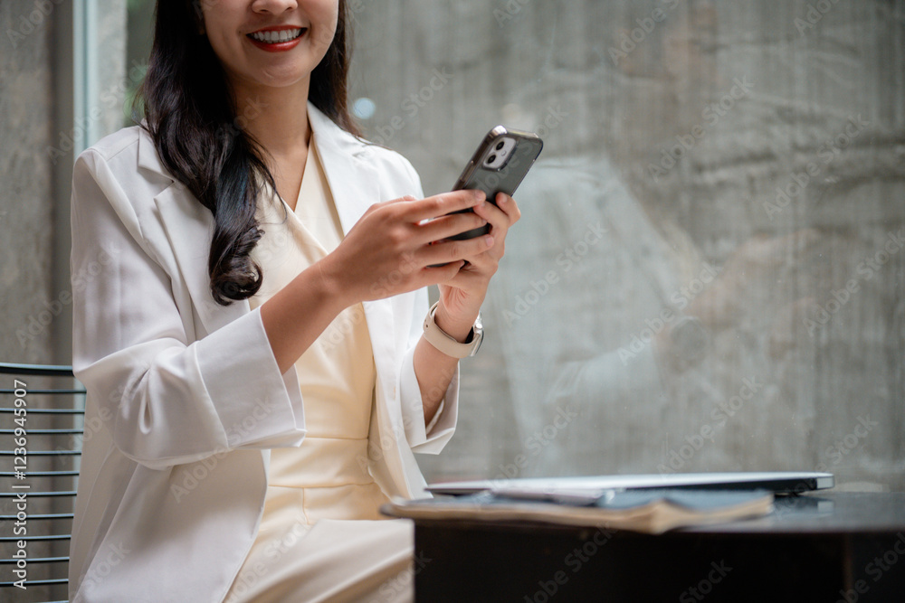 Poster businesswoman smiling while using smartphone and sitting at table with laptop and notebook