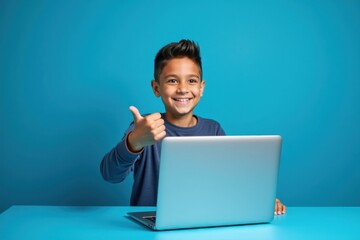 Boy is sitting at table with laptop and giving thumbs up