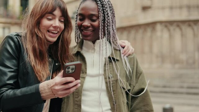 Multiethnic lesbians, two women or friends scrolling through their social media feeds together, watching video content, using cellphone and laughing
