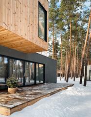 Two-storey timber-clad house in pine forest on a sunny day. Modern house with porch in winter forest. 
