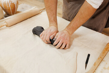 Faceless shot of craftsman pressing clay near wooden tools in workshop