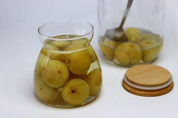 Brine pickled Indian gooseberries in glass bottle, surrounded by fresh gooseberries