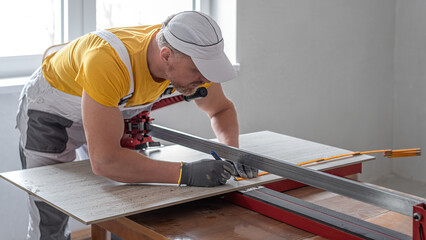 Worker measures and marks the line before cutting the tile on the tile cutter.