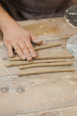 Close up of ceramist rolling clay on wooden table 