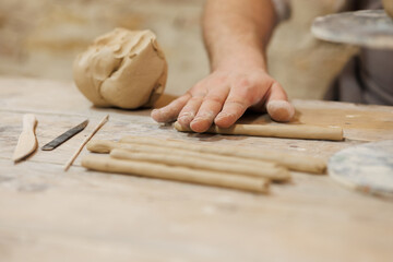 Close up of potter rolling clay near tools on table in workshop