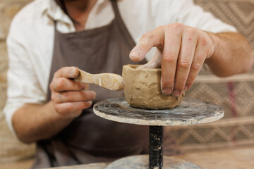 Cropped shot of potter modeling clay with wooden tool in studio