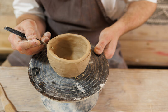 Cropped view of artisan making clay cup with fettling knife in workshop