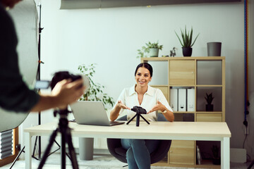 Young Woman Filming Content in Office with Laptop and Camera Equipment