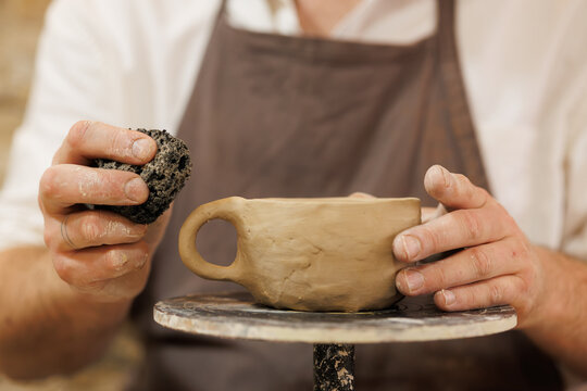 Partial shot of artisan holding sponge near clay cup in studio