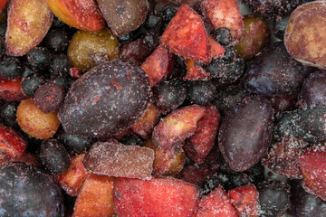Frozen mixed fruits and berries as background, top view. Black plum, grapes, apples, mountain ash, grapes.