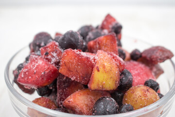 Frozen mixed fruits and berries in a glass bowl on wooden background. Black plum, grapes, apples, mountain ash, grapes.