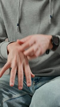Close-up of man scratching his wrist while sitting on couch. Skin irritation or allergic reaction