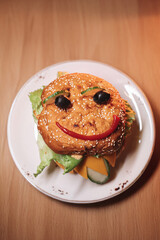 juicy children's burger with a painted face made of ketchup, olives and cucumber, burger with chicken cutlet and beef