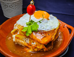 Francesinha - typical Porto sandwich with with pork, smoked sausage, bacon, beef steak and a fried egg, covered in cheesy sauce. Portuguese cuisine.