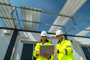 Two engineers in high visibility jackets discussing plans on a laptop at a modular construction site. A window reflection shows their teamwork and professionalism in site planning and management.