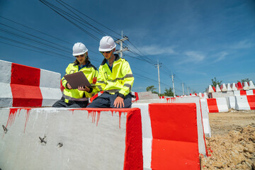 Two engineers wearing high visibility jackets discuss construction progress near concrete...