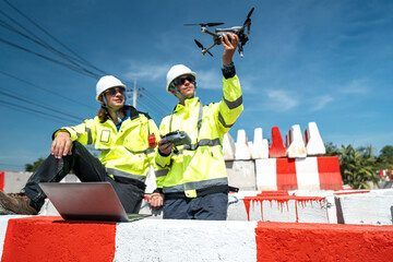 Two engineers in reflective jackets and helmets sit amidst red-and white barricades at a...