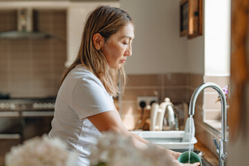 Woman washing dishes in a bright, modern kitchen during the day