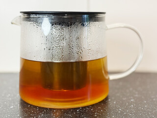 Pouring Hot Water into a Glass Teapot for Brewing Tea. High quality photo Boiling water is poured from a stainless steel kettle into a glass teapot with a metal infuser. The tea leaves begin to steep