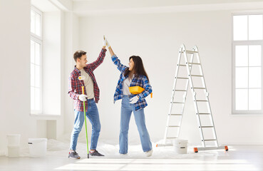 Obraz premium Positive couple collaborates during the renovation of new home, giving a high five while painting walls. Their teamwork and collaboration reflect a shared effort in construction tasks.