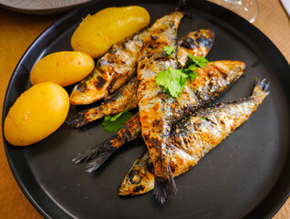 Grilled sardines with young potatoes on a black plate at a restaurant in Portugal