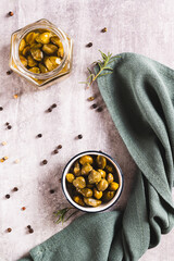 Marinated capers in a bowl, rosemary and peppercorns on the table top and vertical view