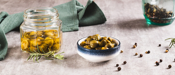 Pickled capers with spices in a bowl and in a jar on the table web banner