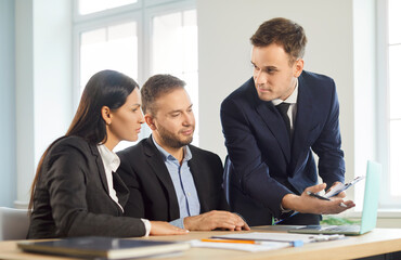 Portrait of a young couple sitting with male business broker or insurance agent showing project on a laptop screen. Clients having consultation with man realtor or financial advisor at office.