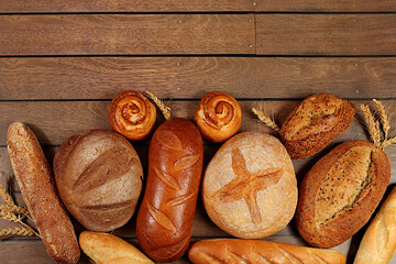 Freshly baked bakery products, whole grain homemade bread, different types of round sourdough bread with crispy crust, baguettes, buns and ears of wheat on wooden background, modern baking concept,