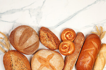 Freshly baked whole grain homemade bread, different types of round sourdough bread with crispy crust, baguettes, buns and ears of wheat on marble background, modern baking concept,