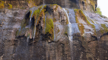 Thin streams of water seep out of the cracks in the rock and fall with a splash downward. The wet...
