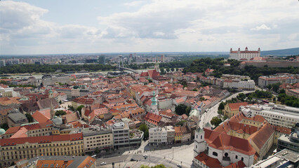 Obraz premium Bratislava city with red-roofed buildings, historic castle, and cloudy sky, aerial view