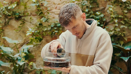 Man adds a new layer of substrate to the glass terrarium. A young gardener creates a florarium at home for a modern interior ,  eco business, crafting