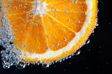 Orange slice submerged in sparkling water creates a refreshing visual in a dark background