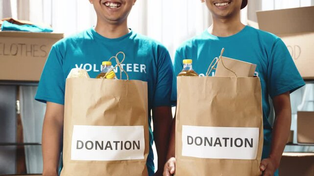 Happy teenage volunteers holding food bags and smiling at the camera in a charity setting. Committed to making a difference in their community through donations. Food donations, charity activities
