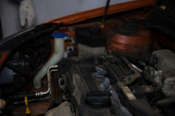 Close-up of car engine with visible spark plugs during maintenance, showing a mechanic's hand in the background, highlighting the process of replacing spark plugs in a garage setting.