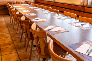 Long table with cutlery and napkins, waiting for the guests to arrive. Rustic and simple setup, with wooden tables and chairs.