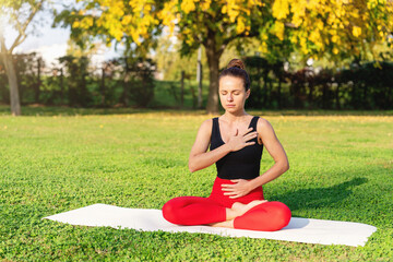 Woman practicing breathing exercise in lotus pose on green grass in city park