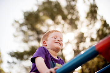 Merry go round, play and smile of boy outdoor in nature for child development, growth or having fun. Balance, happy and youth with excited kid on carousel from below for playground adventure