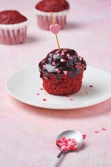 Mini cupcake Red velvet with chocolate glaze and sugar sprinkle hearts on a white plate on a pink concrete background.