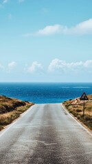 Fototapeta premium Coastal Road Leading to Ocean Under Clear Blue Sky and Clouds