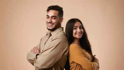 A young married Arab couple stands back to back in a studio against a light background. They exude joy and confidence, showcasing their connection and love in a simple yet elegant manner.