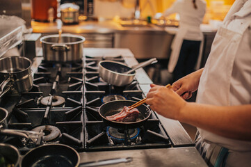 A skilled chef is diligently cooking various types of meat in a frying pan that is placed on top of a stove, creating delicious dishes