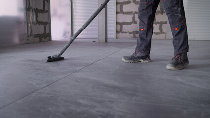 Obraz premium Professional janitor using industrial vacuum cleaner while cleaning expansive grey tiled floor inside public indoor space, systematically removing dust and debris