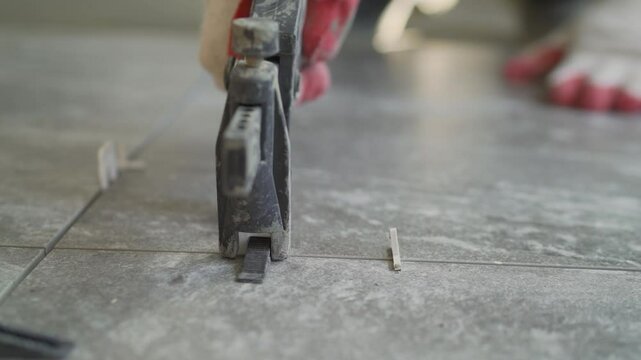 Professional tiler placing wedges into clips of a tile leveling system during floor tiling work