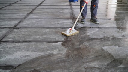 Professional construction worker meticulously cleaning marble tile floor using sponge and bucket, maintaining hygienic workspace during renovation project